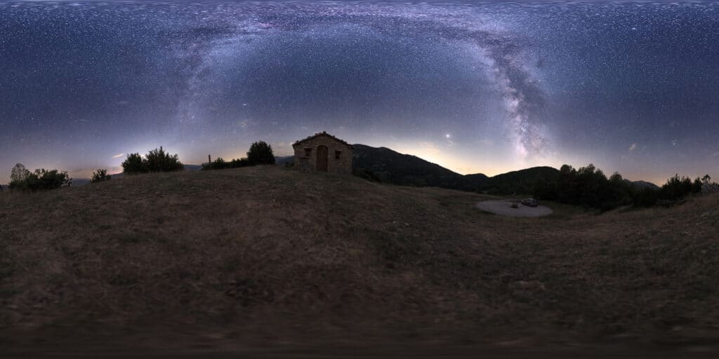 fotografia nocturna 360º donde se ve el primer plano con una ermita y el cielo con el arco de la vía láctea